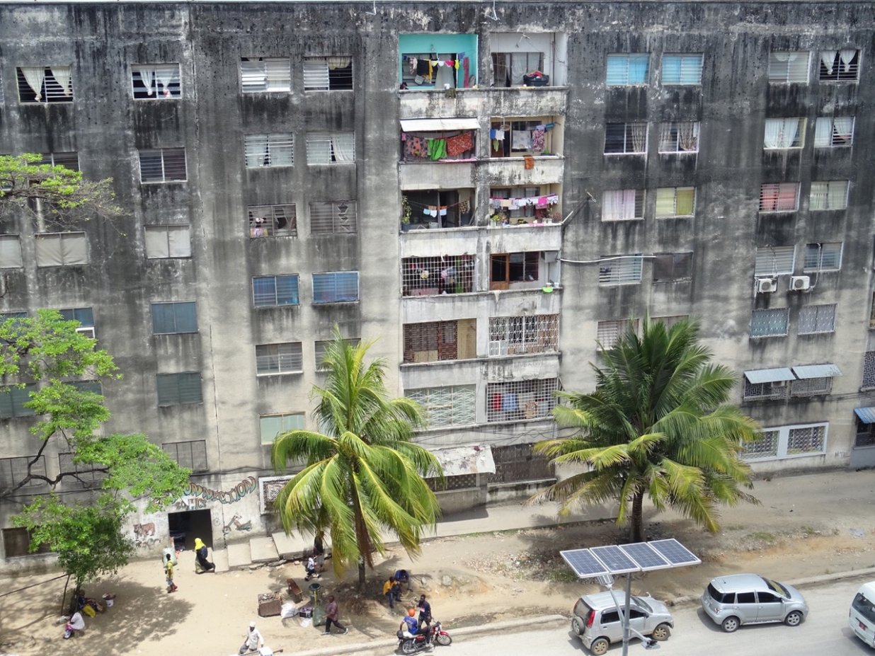 Die Fassade eines Plattenbaus in Sansibsar und ein Ausschnitt der davorliegenden Stra&szlig;e mit Autos und Palmen | © Sarah-Marleen Methner